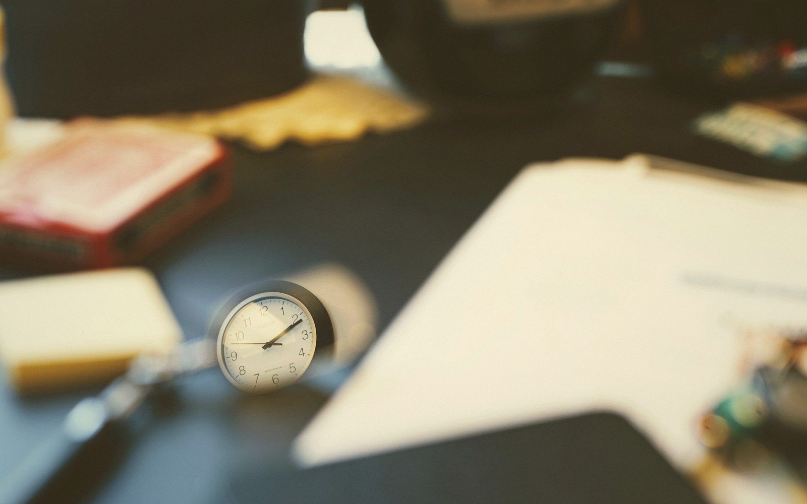 Small clock face resting on a cluttered desk beside papers and a matchbox